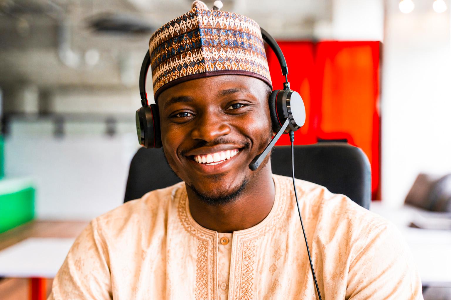 A smiling customer service representative wearing a headset and traditional cap