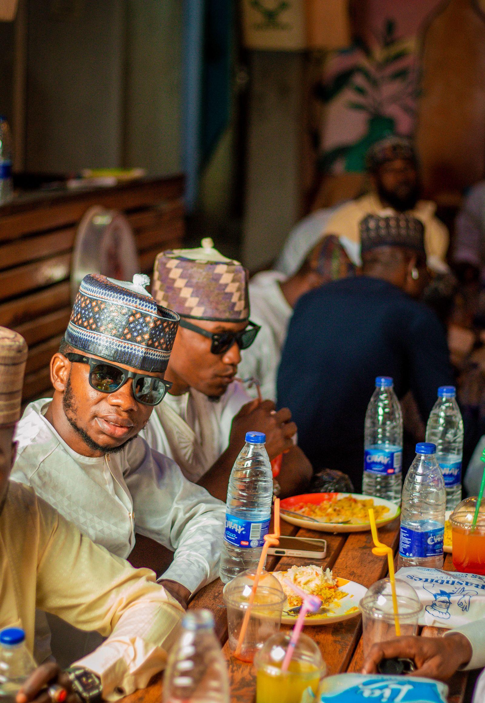 Friends in traditional Hausa caps sharing a meal at a restaurant table