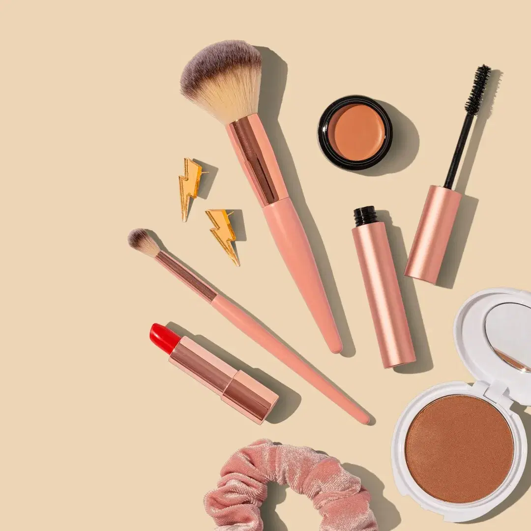 A flat lay of makeup brushes, lipstick, mascara, and a bronzer compact