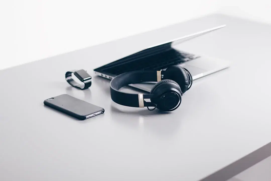 A laptop, wireless headphones, smartwatch, and smartphone on a desk