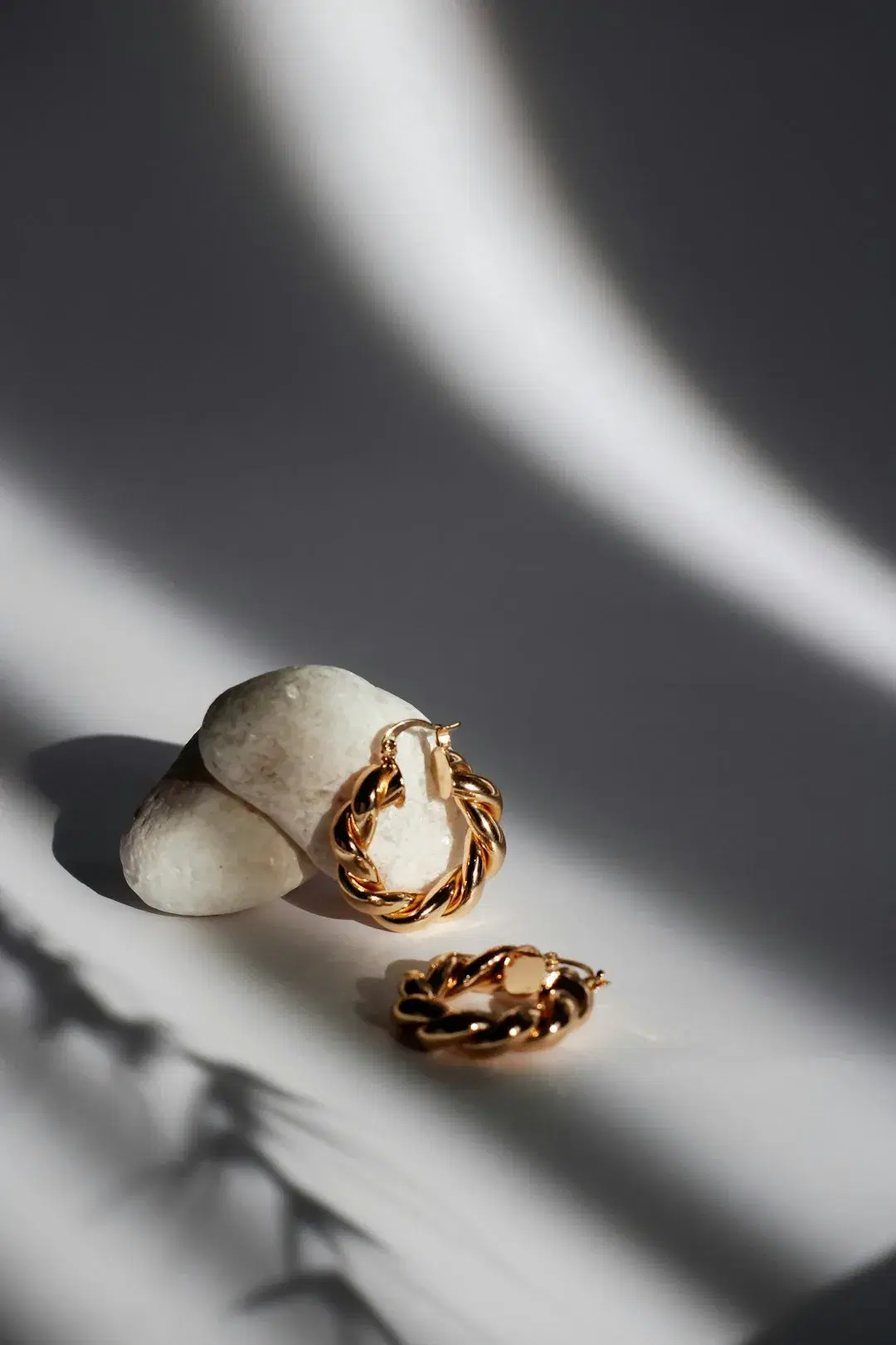 Gold twisted hoop earrings resting on a white stone